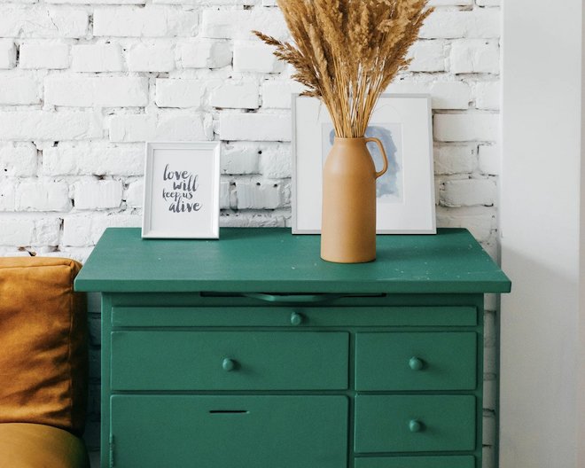 Photo of a green cabinet with a vase and two picture frames on top